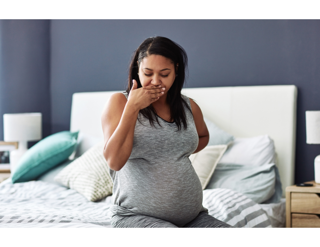 Pregnancy Nausea, pregnant lady sitting on bed with her hand on her mouth feeling nauseous