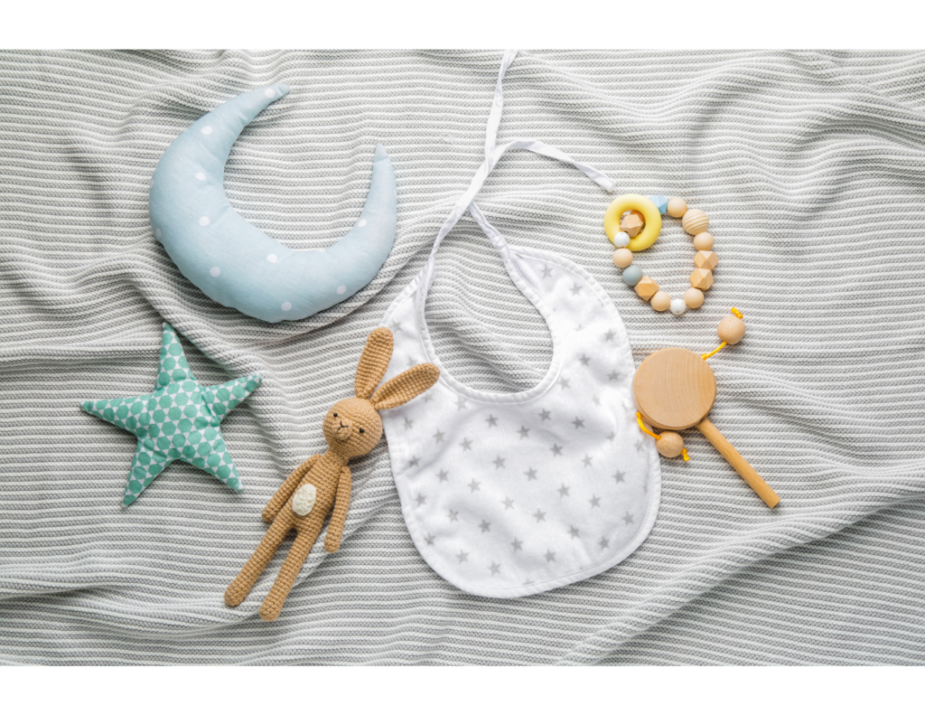 Baby Items - baby rattle, bib, teether, and stuffies, on a grey baby blanket